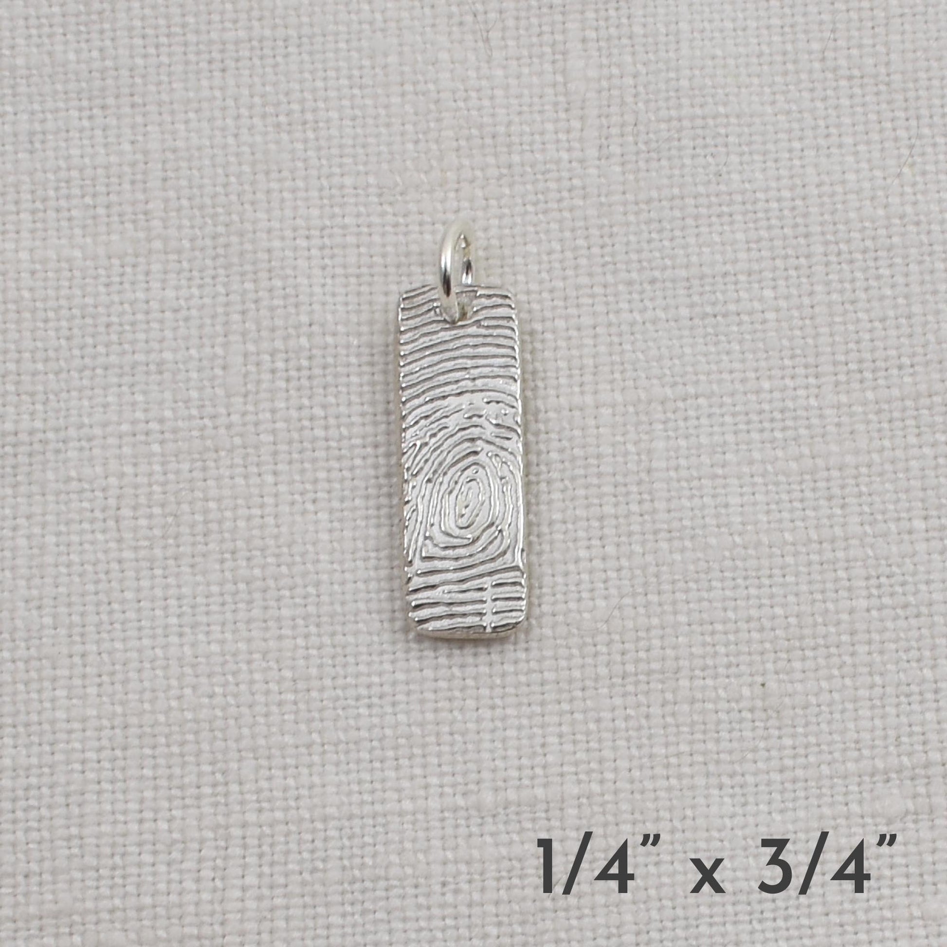Silver pendant on a light beige fabric background with dimensions indicated.