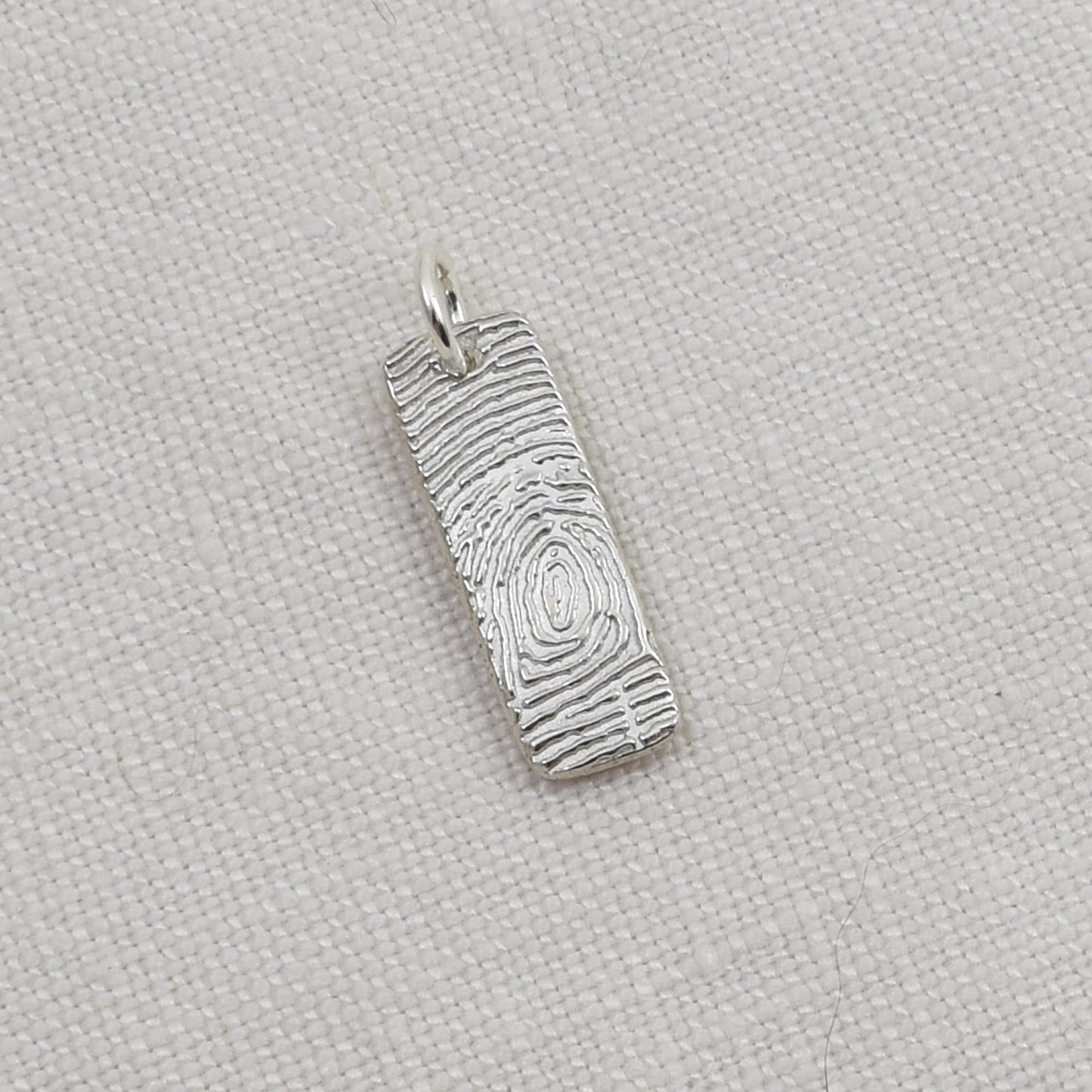 Silver pendant with textured design on a light beige fabric background