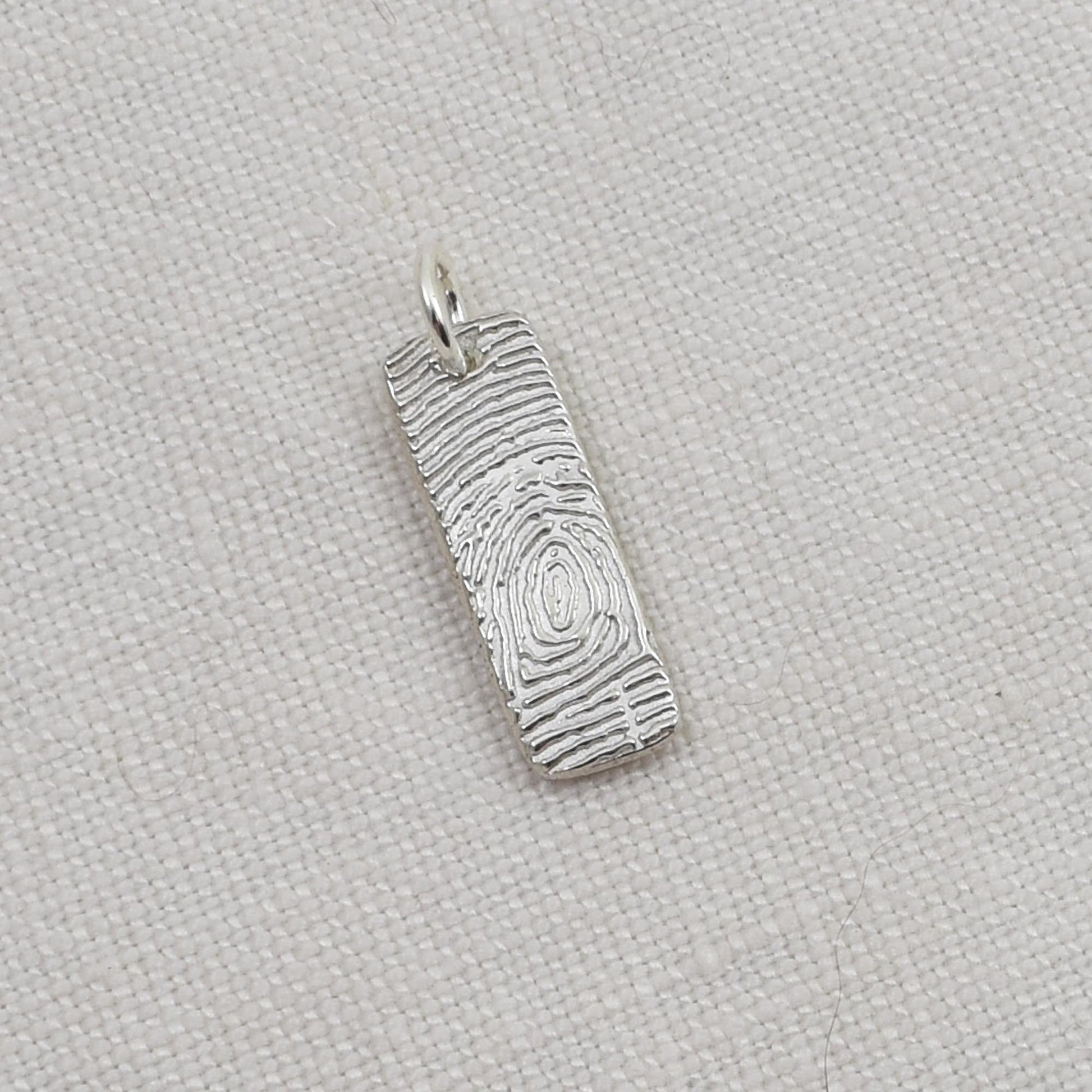 Silver pendant with textured design on a light beige fabric background