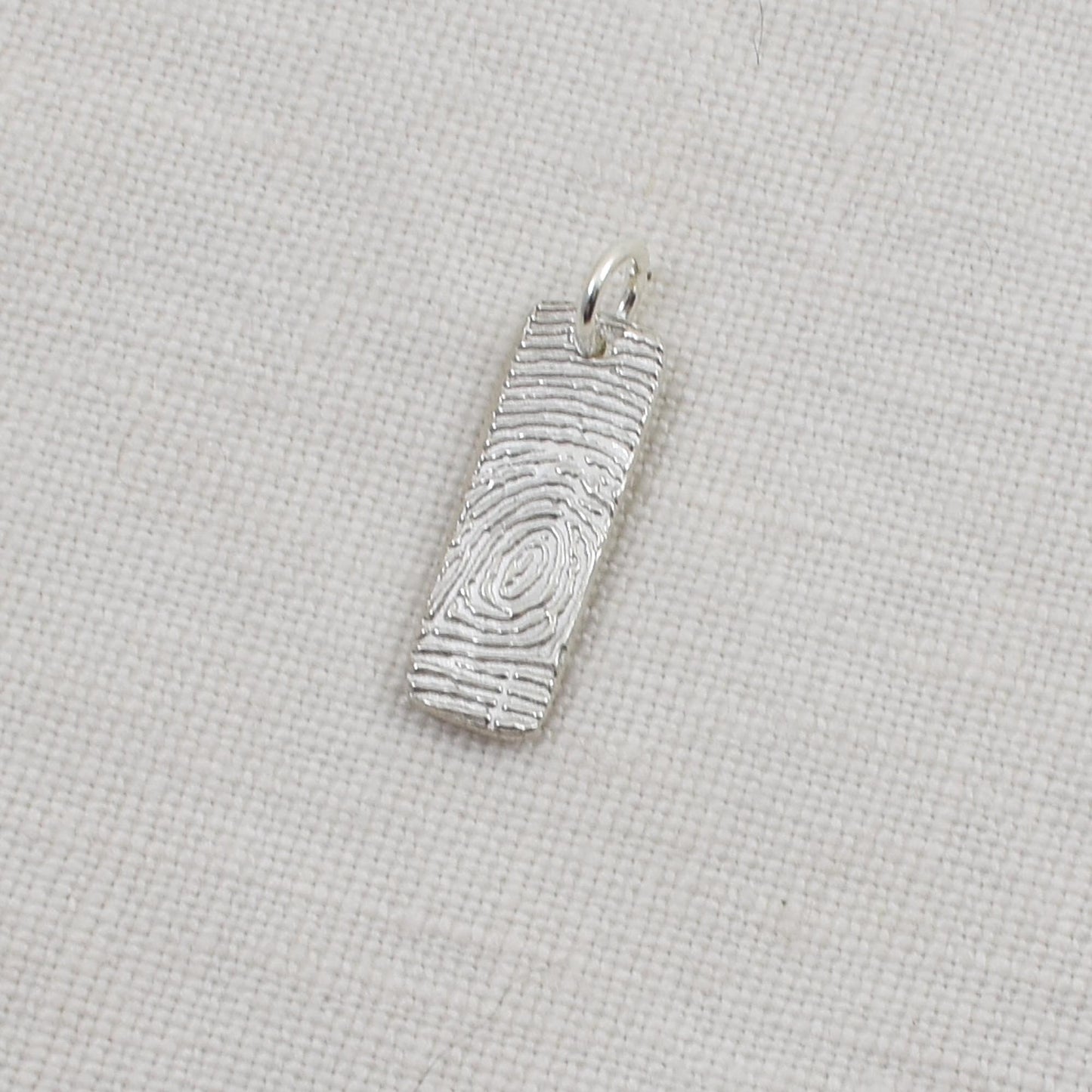 Silver fingerprint pendant on a light beige background