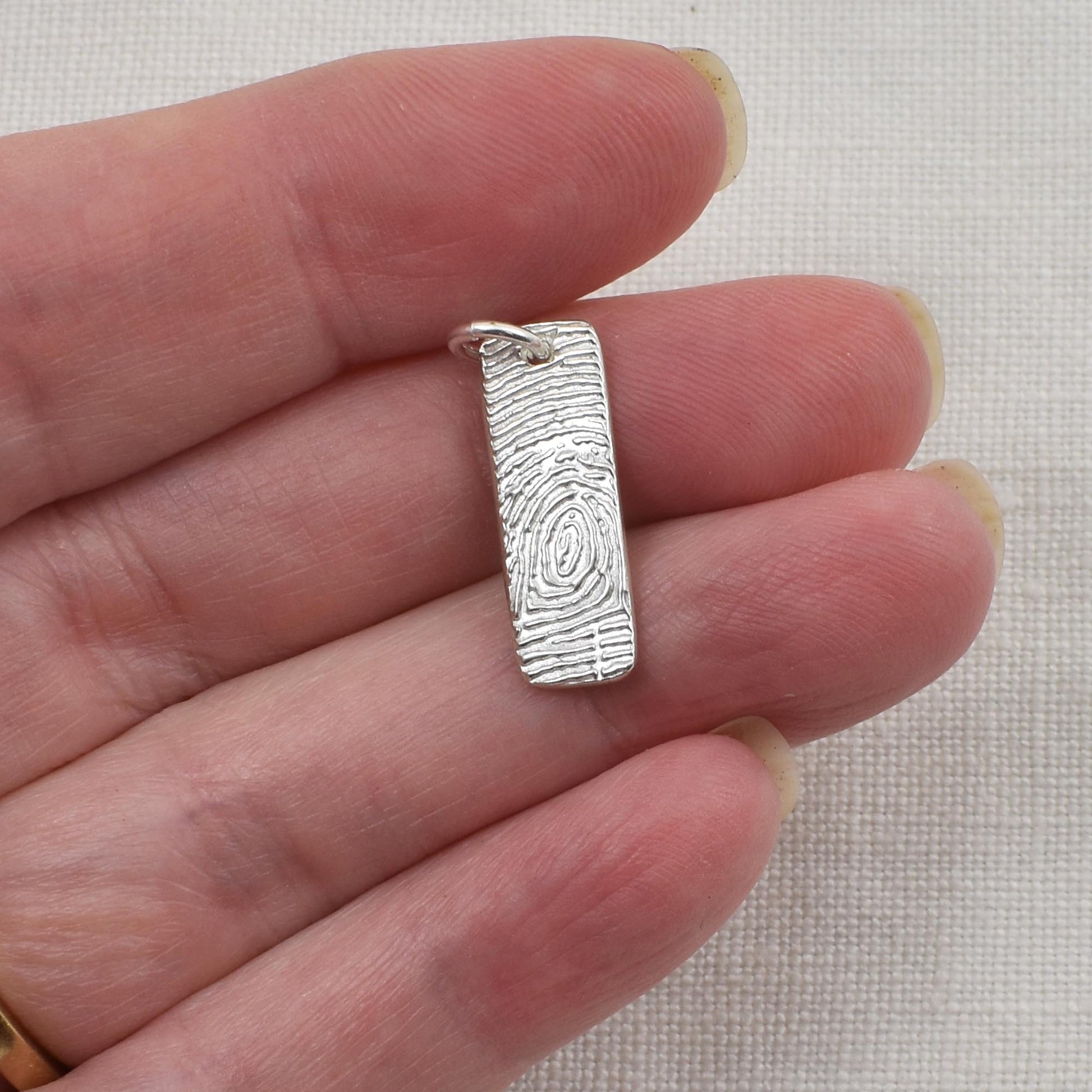 Silver fingerprint pendant held between fingers on a neutral background
