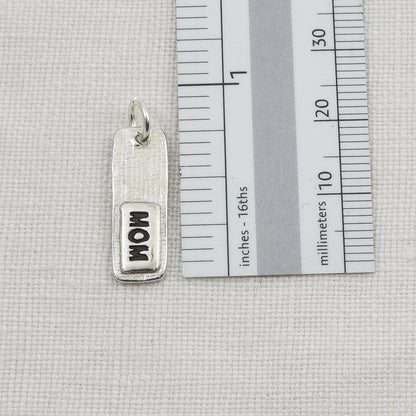 Back of silver fingerprint pendant showing 'MOM' engraving next to a ruler for scale