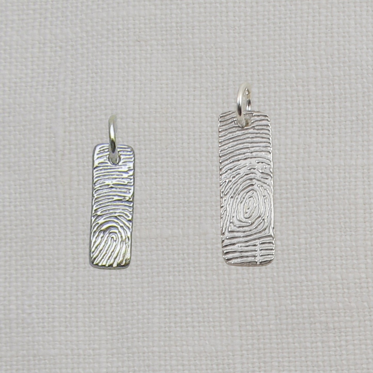 Two silver fingerprint pendants on a textured beige background