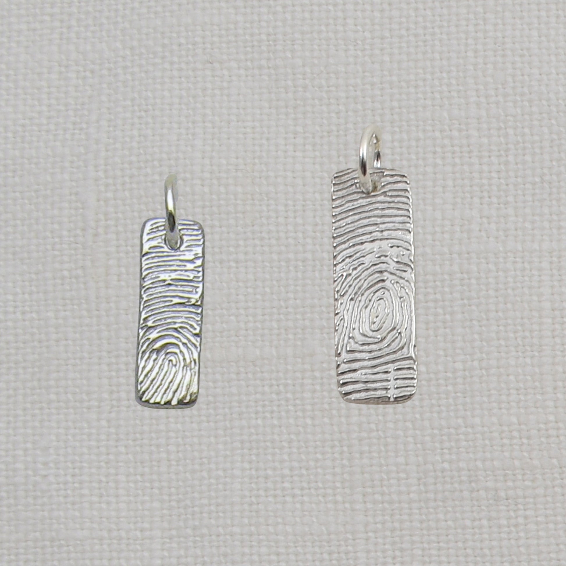 Two silver fingerprint pendants on a textured beige background