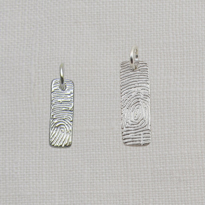 Two silver fingerprint pendants on a textured beige background