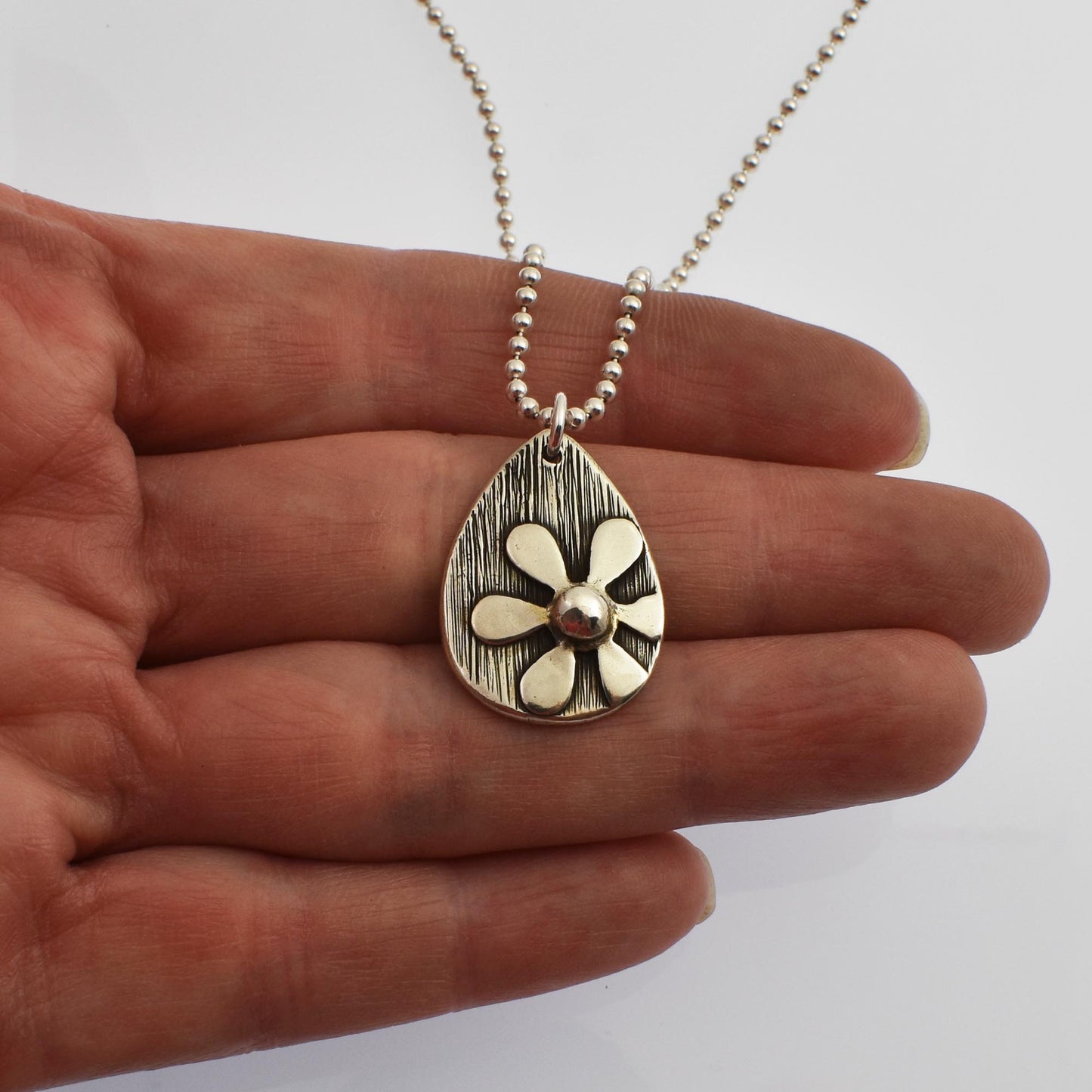 Silver Daisy Flower Teardrop Necklace shown on hand for size reference