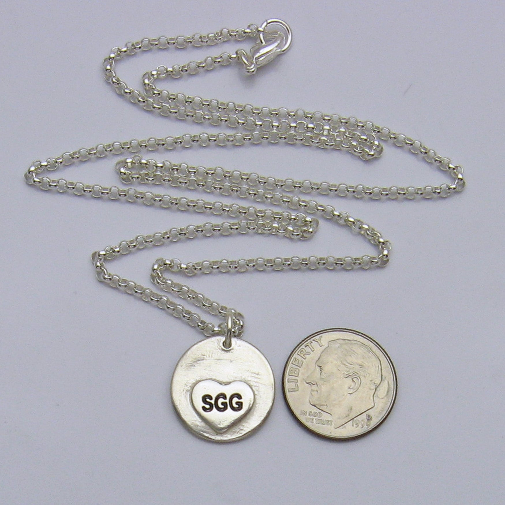 Back of Circle Footprints Necklace showing small heart engraved with initials and next to a dime for size reference