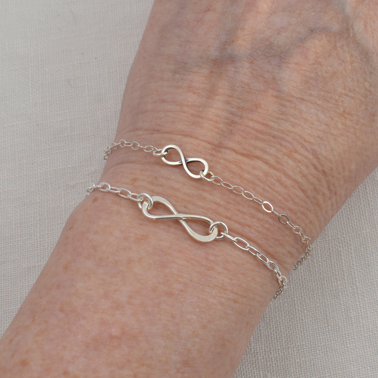 Sterling Silver Infinity Bracelets are shown together being worn on a wrist.