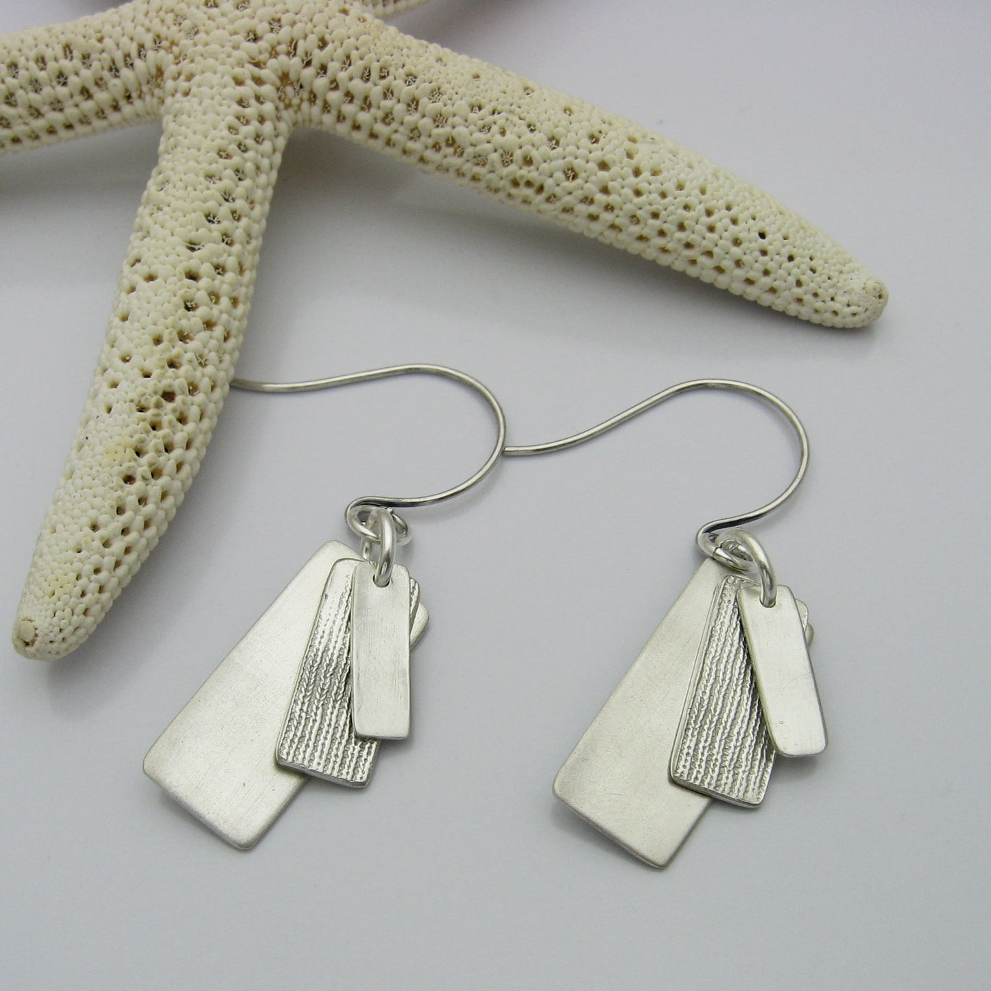 Silver Rectangle Earrings layered with graduating sizes.  The top and bottom layers are matte silver and the middle layer is textured silver.  