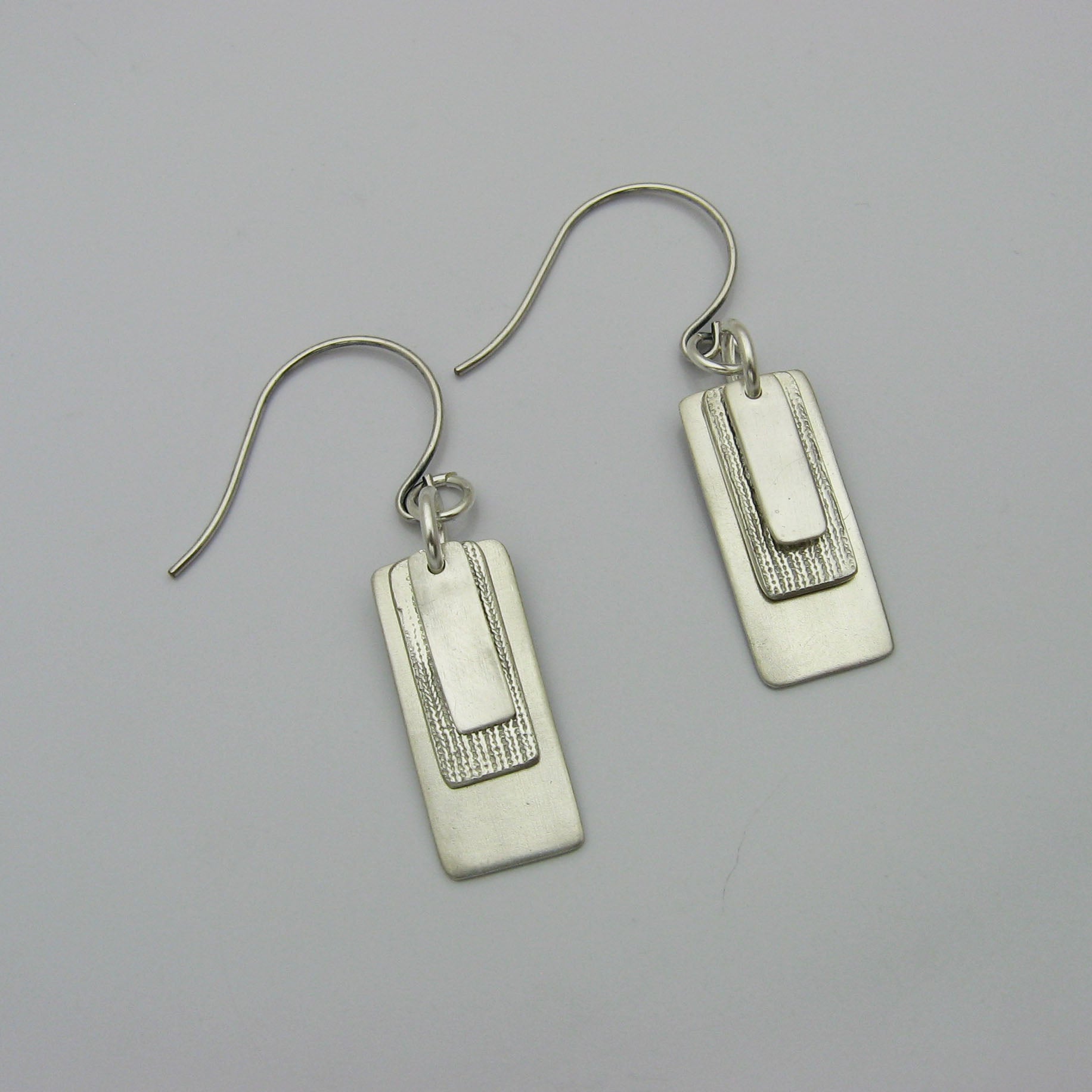 Silver Rectangle Earrings layered with graduating sizes.  The top and bottom layers are matte silver and the middle layer is textured silver.  