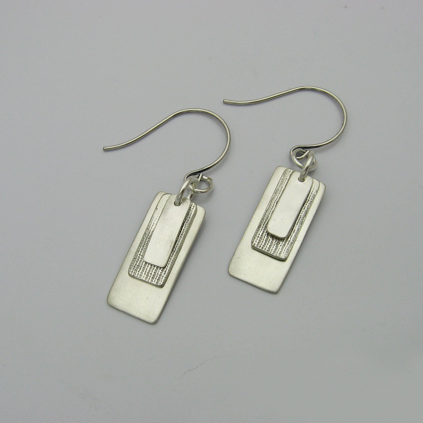 Silver Rectangle Earrings layered with graduating sizes.  The top and bottom layers are matte silver and the middle layer is textured silver.  