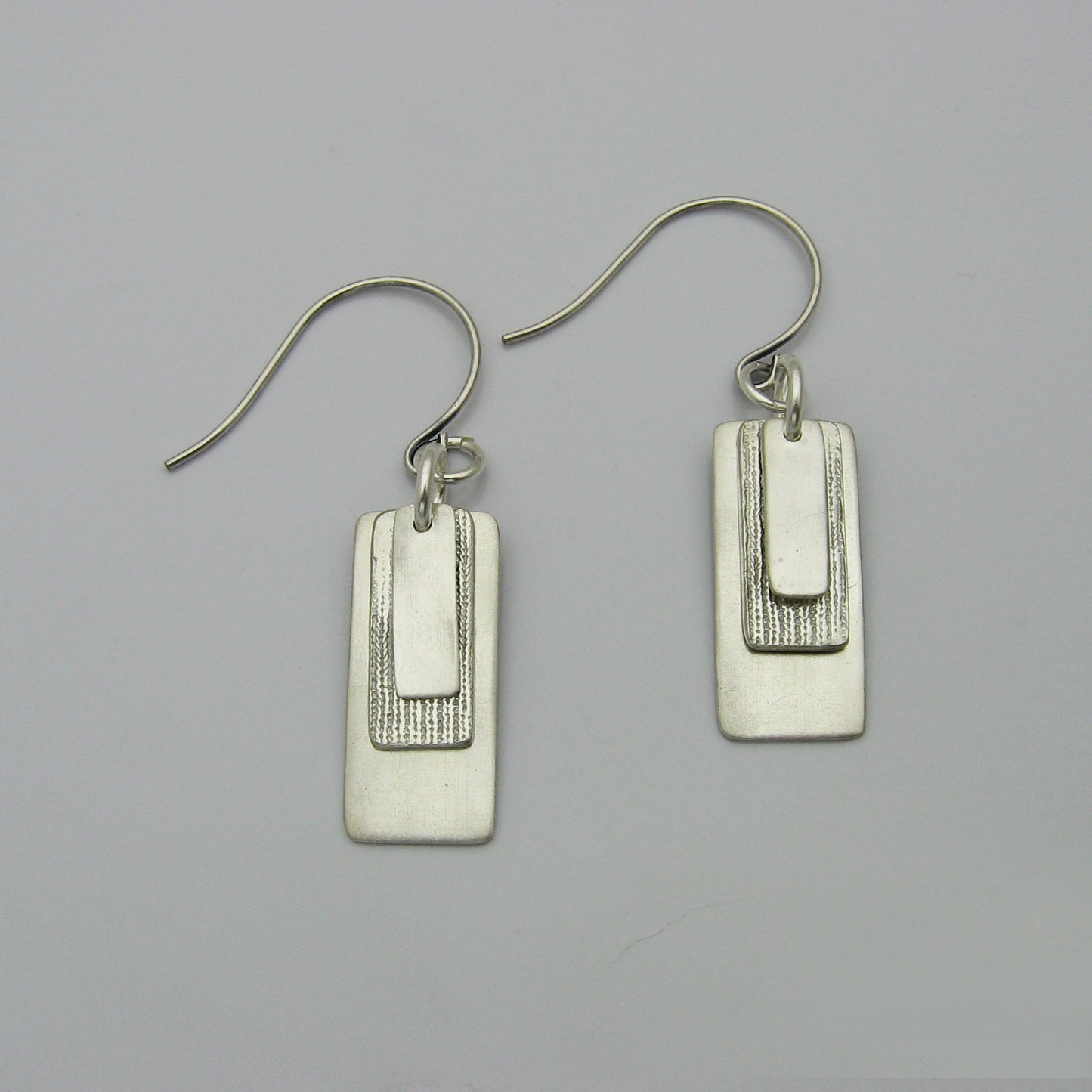 Silver Rectangle Earrings layered with graduating sizes.  The top and bottom layers are matte silver and the middle layer is textured silver.  