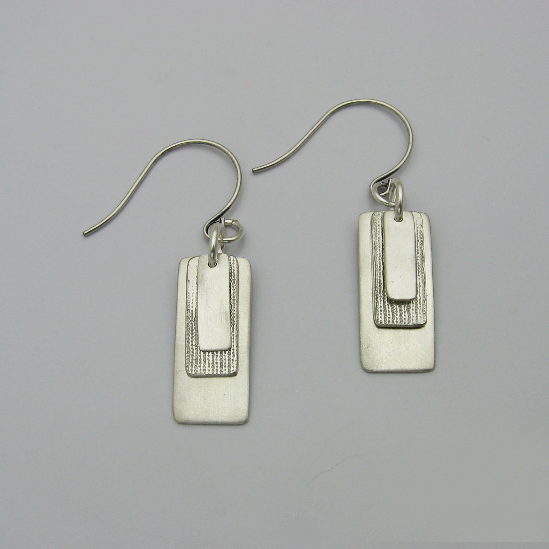 Silver Rectangle Earrings layered with graduating sizes.  The top and bottom layers are matte silver and the middle layer is textured silver.  