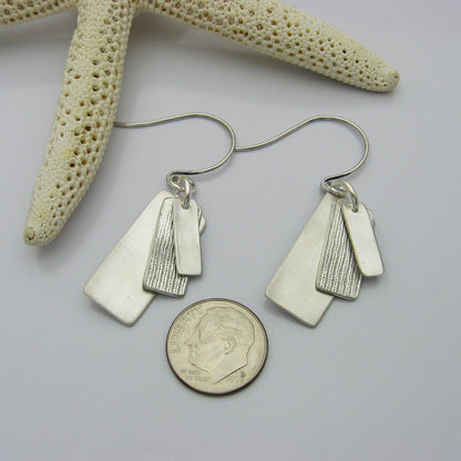Silver Rectangle Earrings layered with graduating sizes.  The top and bottom layers are matte silver and the middle layer is textured silver.  The earrings are shown next to a United States Dime for size reference.