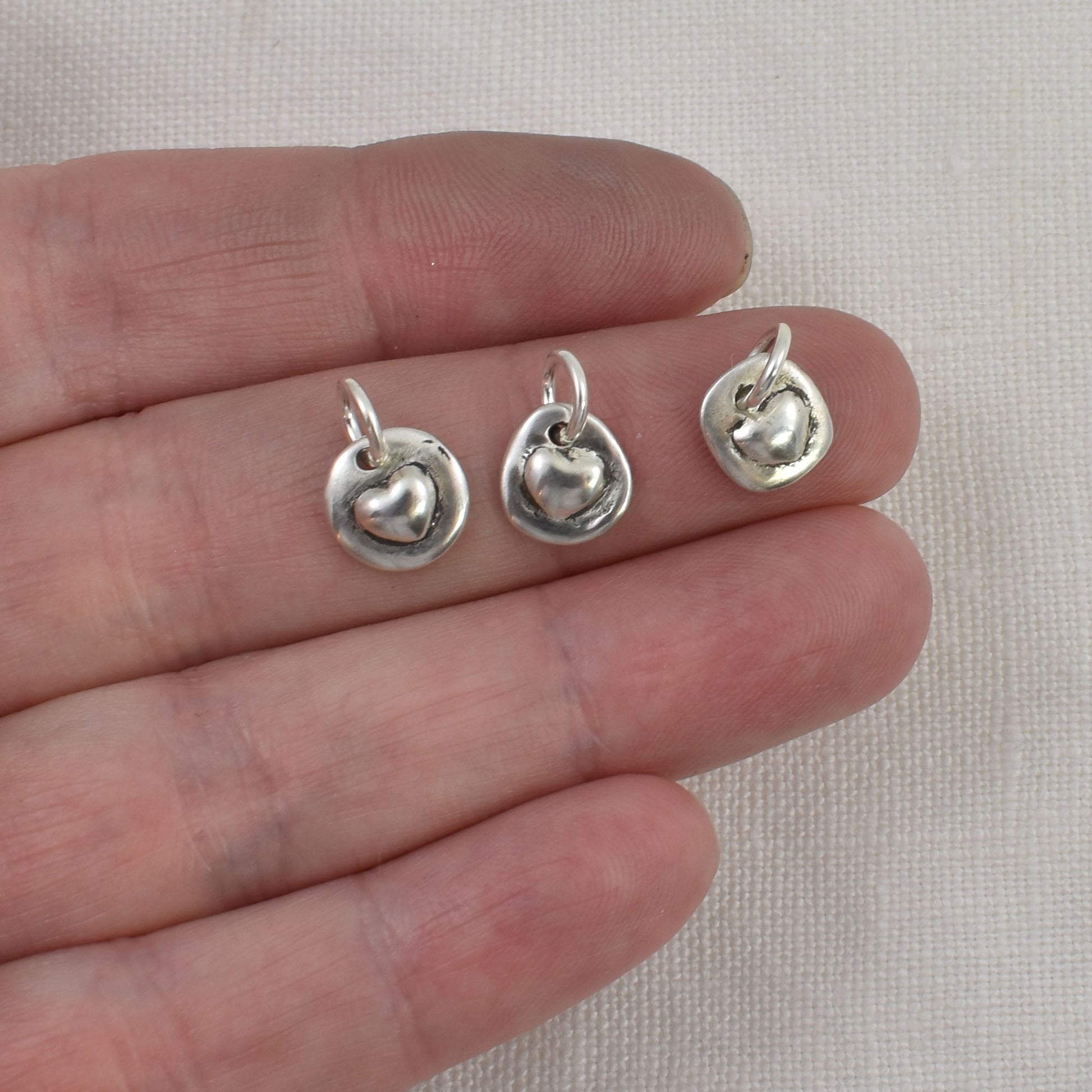 3 Tiny Sterling Silver Heart Charms shown on a finger for size reference