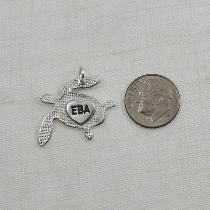 Back of Sterling Silver Sea Turtle Fingerprint Pendant showing small heart engraved with 3 initials.  Shown next to a United States dime for size reference