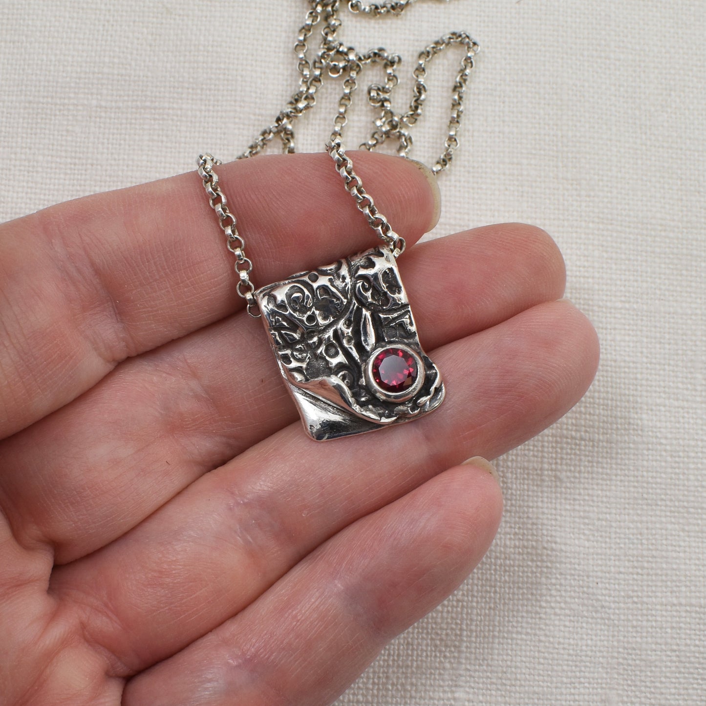 Silver and Ruby Cubic Zirconia Ember Fold Necklace shown on a hand for size reference